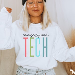 Könnte beinhalten: Weißer Pullover mit dem Text "emergency room TECH" in bunten Buchstaben. Die Buchstaben sind schwarz umrandet.