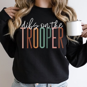 Puede incluir: Sudadera negra con el texto "Dibs on the TROOPER" en letras de colores.