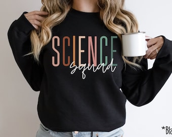 Puede incluir: Sudadera negra con el texto "SCIENCE squad" en letras verticales de colores. Las letras son en tonos de rosa, naranja, marrón y verde.