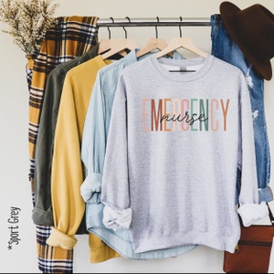 May include: A gray sweatshirt with the text "EMERGENCY nurse" in colorful letters. The letters are stacked vertically and the word "nurse" is written in cursive.