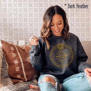 May include: A dark heather grey sweatshirt with a gold graphic of a zodiac symbol, an arrow and bow, and the words "Sagittarius" and "Nov 22 - Dec 21".