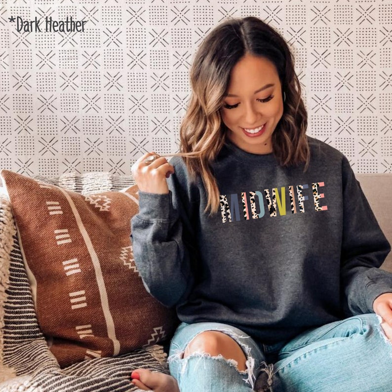 Pode incluir: Uma camisola de cor cinza escura com o termo "MIDWIFE" impresso em letras coloridas com um padr&atilde;o de leopardo.