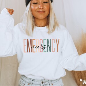 May include: White sweatshirt with the text "EMERGENCY nurse" in colorful vertical stripes.