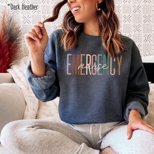 May include: Dark heather grey sweatshirt with the text "EMERGENCY nurse" in colorful letters.