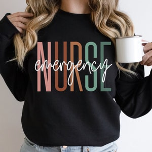 May include: Black sweatshirt with the text "emergency nurse" in colorful vertical letters.