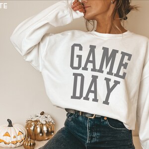 K&ouml;nnte beinhalten: Wei&szlig;er Pullover mit dem Text "GAME DAY" in grauen Buchstaben.