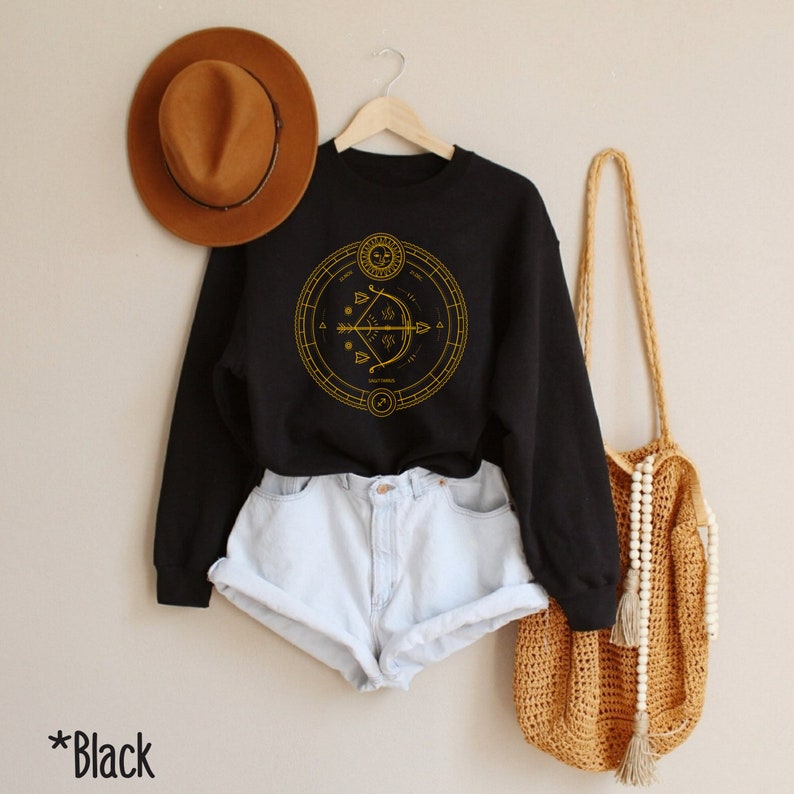 May include: Black sweatshirt with a gold Sagittarius zodiac symbol design. The symbol is a circle with an arrow and other astrological symbols inside.