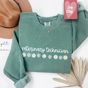 May include: Light green sweatshirt with the text "veterinary technician" and a row of white daisies.
