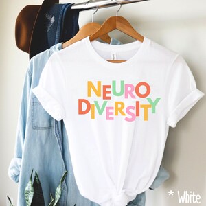 May include: White t-shirt with the words "NEURO DIVERSITY" in colorful block letters.