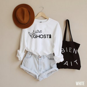 K&ouml;nnte beinhalten: Wei&szlig;es Sweatshirt mit dem Text "future ghost" und einer Geistergrafik. Das Sweatshirt wird mit hellblauen Jeans-Shorts und einem braunen Fedora getragen.