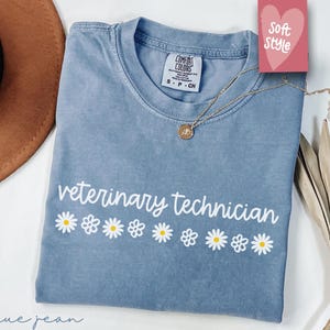 May include: A blue jean t-shirt with the text "veterinary technician" in white script with a row of white daisies underneath. The shirt is made of a soft, comfortable fabric.