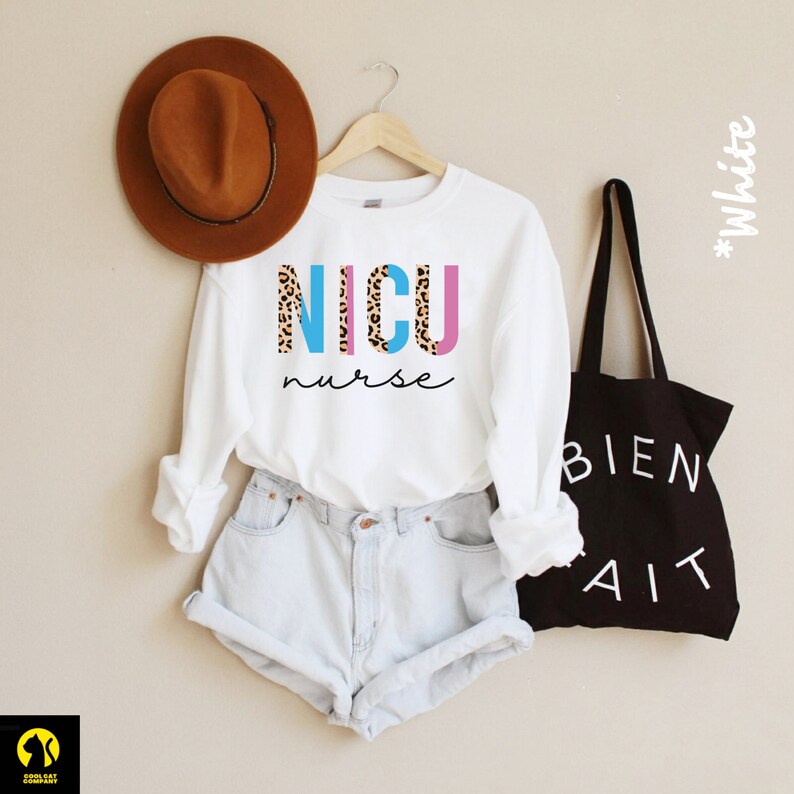 May include: White long-sleeved shirt with the text "NICU nurse" in blue, pink, and brown leopard print letters.