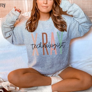 May include: A grey sweatshirt with the text "X-RAY TECHNOLOGIST" in colourful letters. The letters are in shades of pink, orange, and green.