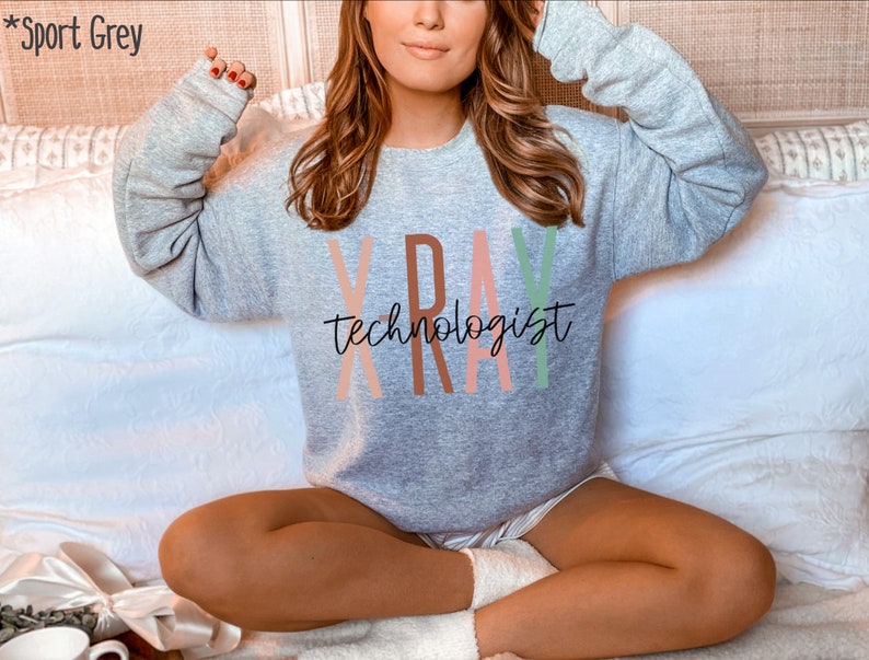 May include: A grey sweatshirt with the text "X-RAY TECHNOLOGIST" in colourful letters. The letters are in shades of pink, orange, and green.