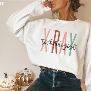 May include: White sweatshirt with the text "XRAY technologist" in colourful letters. The letters are in shades of pink, brown, and green.