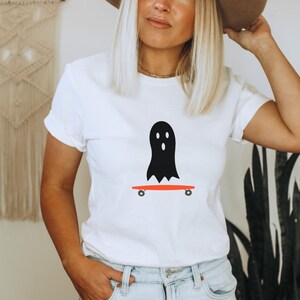 Peut inclure: T-shirt blanc avec un motif de fant&ocirc;me noir sur un skateboard rouge. Le fant&ocirc;me a trois trous pour les yeux. Le skateboard a des roues noires. Ce t-shirt d&eacute;contract&eacute; est adapt&eacute; au quotidien. Le design a un th&egrave;me d'Halloween.