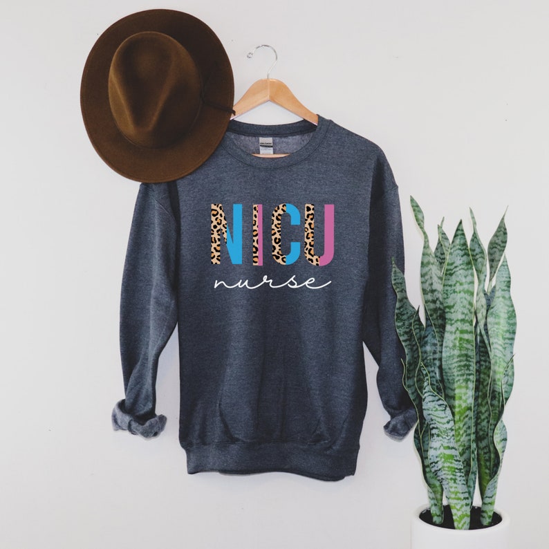 May include: A dark gray sweatshirt with the words "NICU nurse" printed on the front. The letters "NICU" are in blue, pink, and yellow with a leopard print pattern.