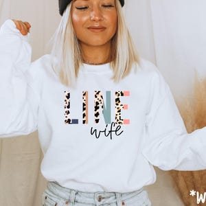 Puede incluir: Sudadera blanca con el texto "LINE wife" en letras de colores con estampado de leopardo.