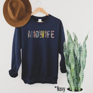 Pode incluir: Camisola azul marinho com a palavra "MIDWIFE" impressa em letras coloridas com um padr&atilde;o de leopardo.