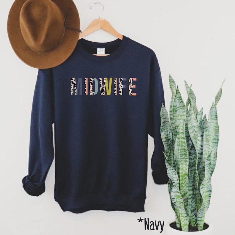 Pode incluir: Camisola azul marinho com a palavra "MIDWIFE" impressa em letras coloridas com um padr&atilde;o de leopardo.