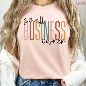 Puede incluir: Una camiseta rosa con el texto "small business owner" en rayas verticales de colores. El texto est&aacute; en una fuente moderna y manuscrita.