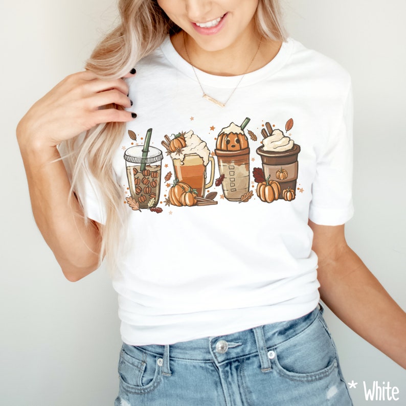 May include: White t-shirt with a graphic of four fall-themed drinks. The drinks are a pumpkin spice latte, a caramel apple cider, a pumpkin spice cold brew, and a pumpkin spice iced coffee. Each drink has a pumpkin and fall leaves around it.