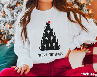 Peut inclure: Sweat-shirt blanc avec un motif de sapin de Noël composé de chats noirs. Le sapin est composé de chats noirs portant des bonnets de Père Noël. Le texte "MEOWY CHRISTMAS" est imprimé sous le sapin.