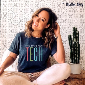 Puede incluir: Una camiseta azul oscuro con el texto "emergency room TECH" en letras de colores. Las letras son rojas, verdes, azules y verde azulado.
