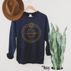 May include: Navy blue sweatshirt with a gold graphic of the Sagittarius zodiac sign, featuring an arrow and a circle with astrological symbols.