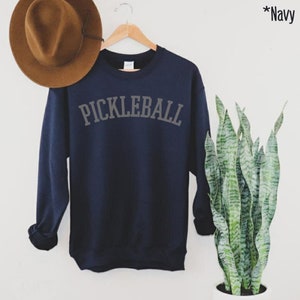 May include: Navy blue sweatshirt with the text "PICKLEBALL" in a grey arch across the front.