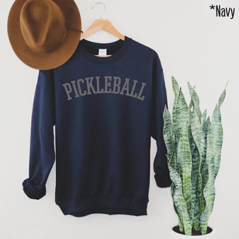 May include: Navy blue sweatshirt with the text "PICKLEBALL" in a grey arch across the front.