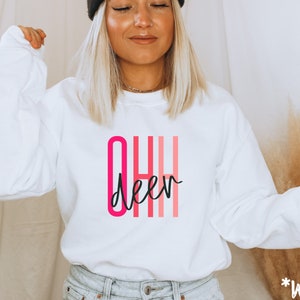 May include: White sweatshirt with a pink and red "OH Deer" graphic.