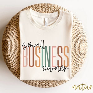 Puede incluir: Una camiseta beige con el texto "small business owner" en letras estilizadas de colores. El texto est&aacute; en un arco&iacute;ris de colores, incluyendo rosa, naranja, marr&oacute;n, verde y azul.