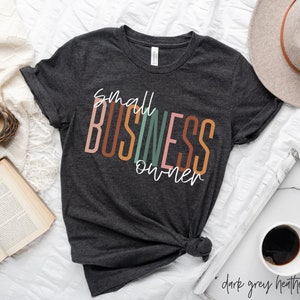 Puede incluir: Una camiseta de color gris oscuro jaspeado con el texto "small business owner" en blanco y letras de colores.