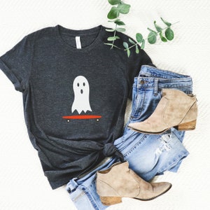 Peut inclure: T-shirt gris fonc&eacute; avec un motif de fant&ocirc;me blanc sur un skateboard rouge. L'ensemble comprend un jean bleu et des bottines beiges. Une branche de verdure est &eacute;galement pr&eacute;sente. Le style est d&eacute;contract&eacute;.