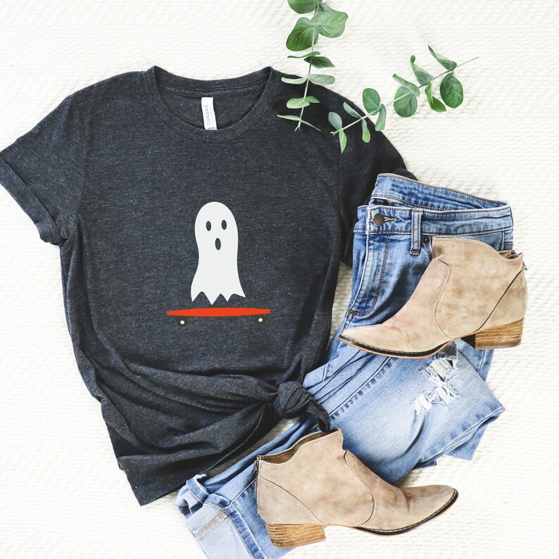 Peut inclure: T-shirt gris fonc&eacute; avec un motif de fant&ocirc;me blanc sur un skateboard rouge. L'ensemble comprend un jean bleu et des bottines beiges. Une branche de verdure est &eacute;galement pr&eacute;sente. Le style est d&eacute;contract&eacute;.