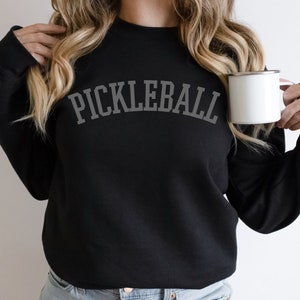 May include: Black sweatshirt with the text "PICKLEBALL" in a grey arch design.