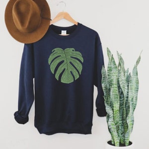 Peut inclure: Un sweat-shirt bleu marine avec un motif de feuille de monstera verte.