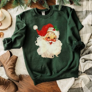 May include: A dark green sweatshirt with a vintage illustration of Santa Claus's face. The illustration is in red, white, and yellow.