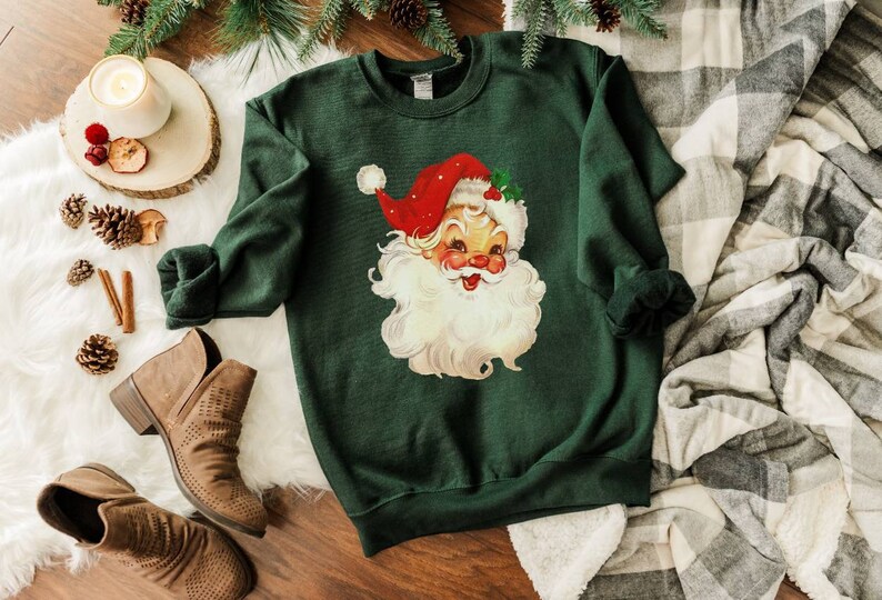 May include: A dark green sweatshirt with a vintage illustration of Santa Claus's face. The illustration is in red, white, and yellow.