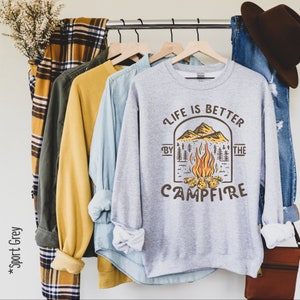 K&ouml;nnte beinhalten: Ein graues Sweatshirt mit einer Feuerstellenszene und dem Text "Life is better by the campfire".
