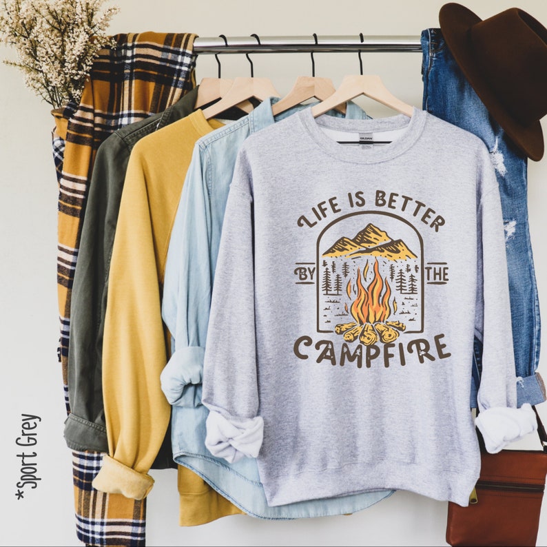 K&ouml;nnte beinhalten: Ein graues Sweatshirt mit einer Feuerstellenszene und dem Text "Life is better by the campfire".