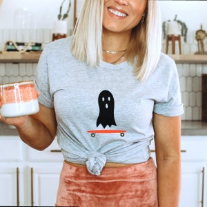 Peut inclure: T-shirt gris clair avec un motif de fant&ocirc;me noir sur un skateboard rouge. Le fant&ocirc;me a trois yeux ovales blancs et une bouche ovale blanche. Le t-shirt est en mati&egrave;re douce, id&eacute;al pour Halloween.