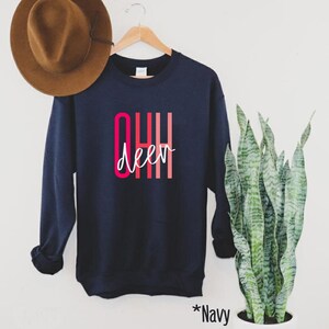May include: Navy blue sweatshirt with the text "OHH deer" in pink and red lettering. The sweatshirt is hanging on a wooden hanger.