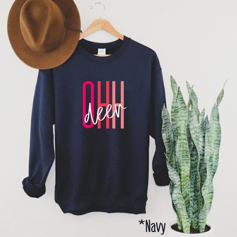 May include: Navy blue sweatshirt with the text "OHH deer" in pink and red lettering. The sweatshirt is hanging on a wooden hanger.