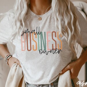 Puede incluir: Una camiseta gris con el texto "small business owner" en letras de colores.