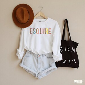 Peut inclure: Sweat-shirt blanc avec le mot "ESQUIRE" imprim&eacute; en lettres color&eacute;es avec un motif l&eacute;opard. Le sweat-shirt est associ&eacute; &agrave; un short en jean et un sac fourre-tout noir avec les mots "BIEN FAIT" imprim&eacute;s en blanc.
