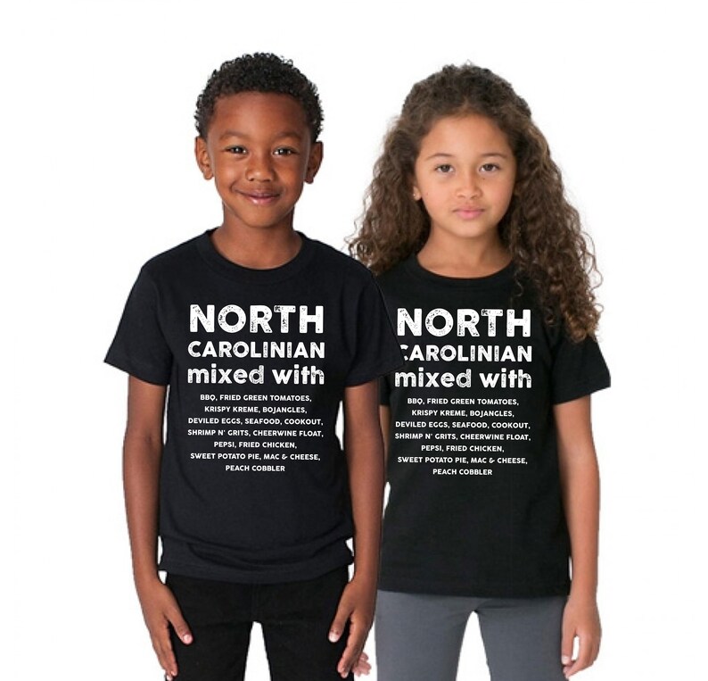 May include: Two children wearing black t-shirts with the text "NORTH CAROLINIAN mixed with" and a list of North Carolina foods in white. The list includes BBQ, fried green tomatoes, and sweet potato pie.