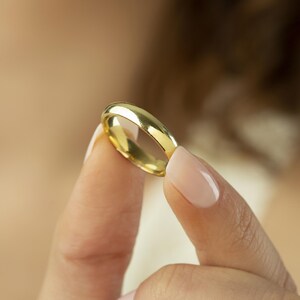 May include: A polished gold band ring with a smooth, rounded surface and a reflective metallic finish. The ring features a simple, continuous circular design with a consistent width throughout, showcasing a bright yellow gold tone and high luster.