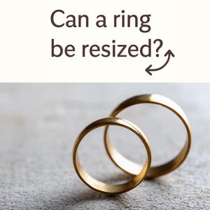 May include: Two gold wedding bands are displayed on a textured gray surface. The rings are circular and shiny, reflecting light. Above the rings, the text "Can a ring be resized?" is written in brown.